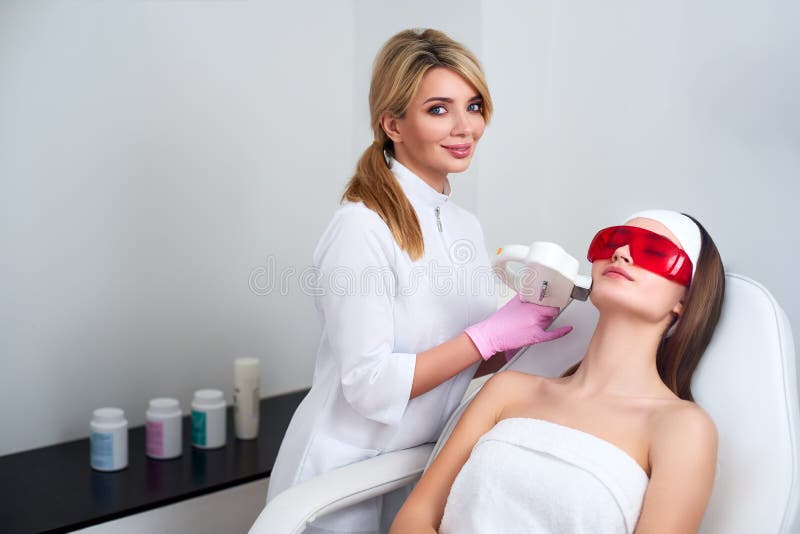 Beautician doctor doing laser RF rejuvenation for pretty young woman face at beauty salon. Elos epilation hair removal stock photography Beautician doctor doing laser RF rejuvenation for pretty young woman face at beauty salon. Elos epilation hair removal stock photography