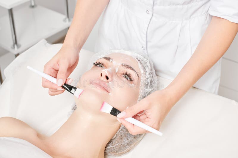 Beautician Rubbing Cream With Brushes Into Woman Face Skin For Rejuvenation Cosmetic Procedure