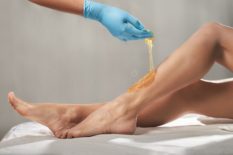 Beautician waxing female legs with liquid sugar paste in spa center.