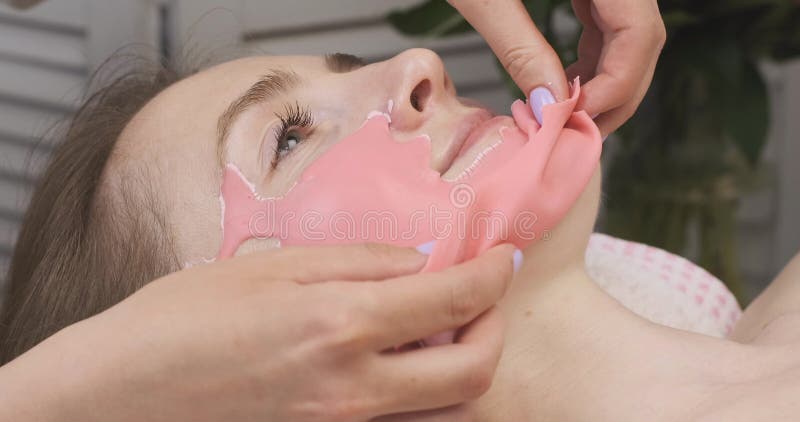 Beautiern tar bort alginat-mask från klientsidan. Ung kvinna vid mottagningen i skönhetsvården.