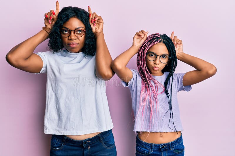 Beautiful african american mother and daughter wearing casual clothes and glasses doing funny gesture with finger over head as