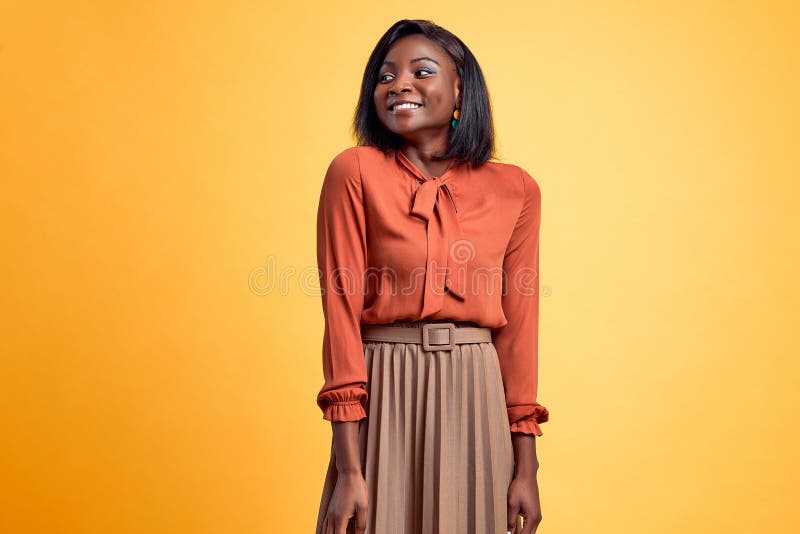 Beautiful african american young girl smiling and posing in stylish blouse and skirt isolated yellow background. Copy space