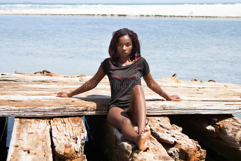 african-american woman in her bikini and t-shirt sitting on a piece of wood on the beach. african-american woman in her bikini and t-shirt sitting on a piece of wood on the beach