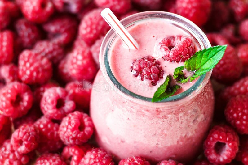Beautiful appetizer pink raspberries fruit smoothie or milk shake in glass jar with berries background, top view.