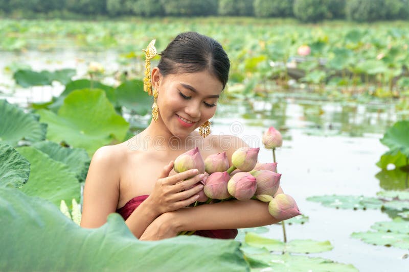 Beautiful asia women wearing traditional Thai dress and sitting on wooden boat in flower lotus lake. Her hands are holding a pink stock photography Beautiful asia women wearing traditional Thai dress and sitting on wooden boat in flower lotus lake. Her hands are holding a pink stock photography