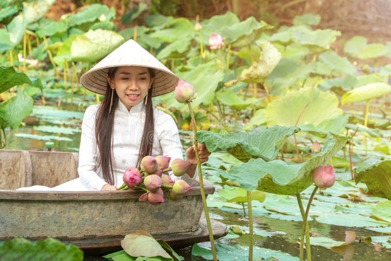 Beautiful asia women wearing white traditional Vietnam dress Ao Wai and Vietnam farmer`s hat and sitting on wooden boat in flow