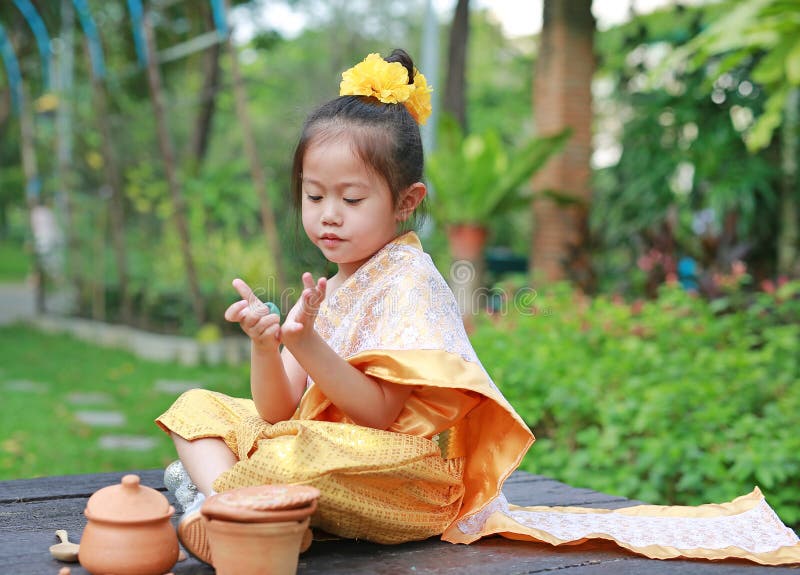 Beautiful Asian child girl in traditional thai dress play making Thai culture dessert in the public garden stock images Beautiful Asian child girl in traditional thai dress play making Thai culture dessert in the public garden stock images