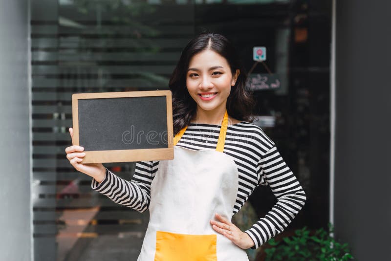 Beautiful asian florist holding blank sign and pointing at copy space.