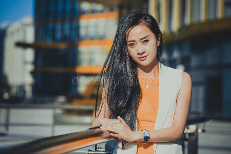 Beautiful Asian girl model in white dress posing at the modern glass style office city background.