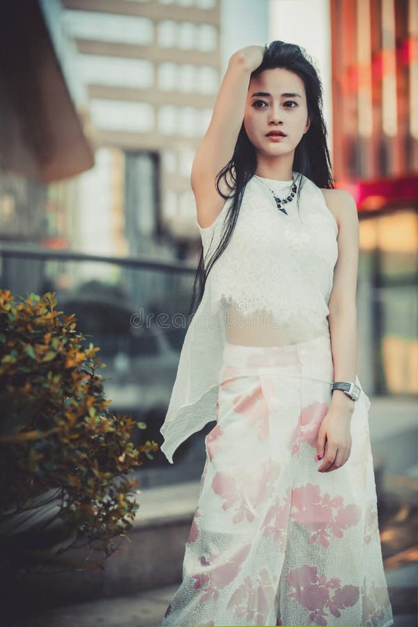 Beautiful Asian girl model in white dress posing at the modern style city park background.