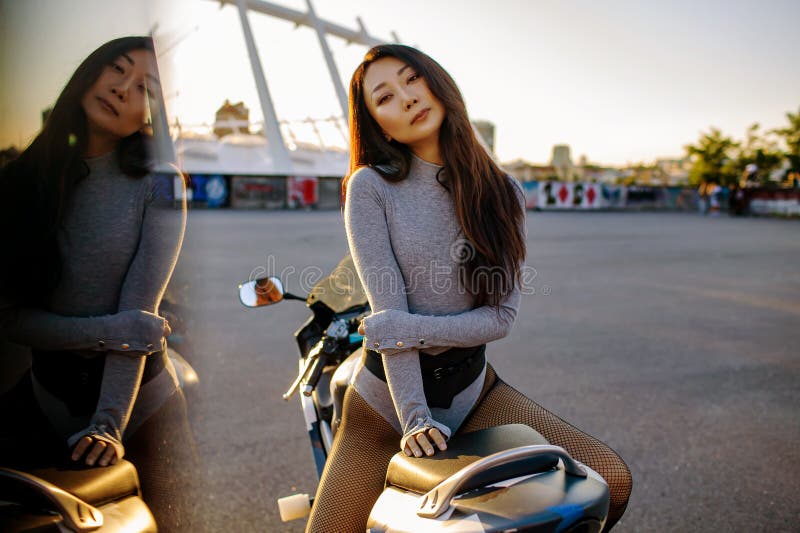 Beautiful Asian Girl Seating On Moto Bike In City. At Sunset