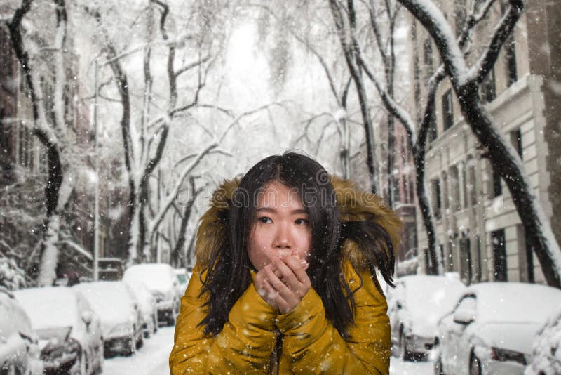 Beautiful Asian Korean woman feeling cold and chilly freezing feeling cold in Winter weather wearing yellow jacket with fur hood. Girl, expression.