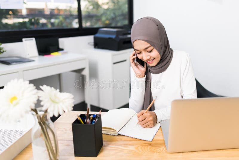 Beautiful Asian Muslim Woman Working Using Laptop and Mobile Phone Call