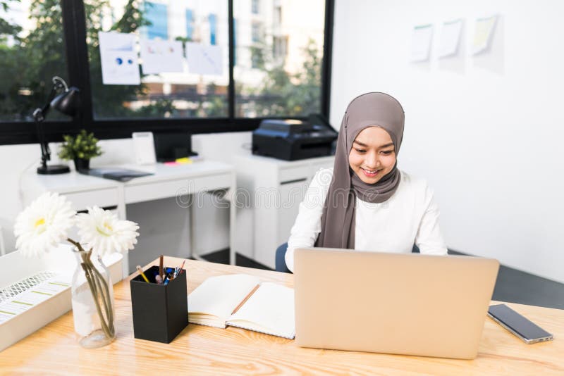 Beautiful Asian muslim woman working using laptop in modern office. Small business company owner, startup entrepreneur concept