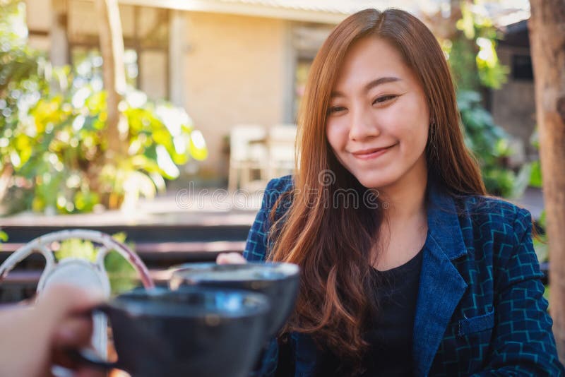 A Beautiful Asian Woman Clinking Coffee Mugs with Friend in Cafe Stock ...