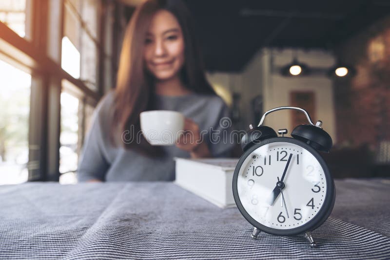 A beautiful Asian woman drinking coffee in the morning with black alarm clock stock photo A beautiful Asian woman drinking coffee in the morning with black alarm clock stock photo