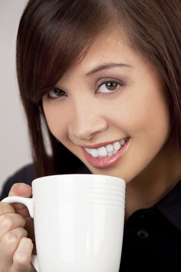 A beautiful young oriental woman with a wonderful toothy smile drinking from a white mug. A beautiful young oriental woman with a wonderful toothy smile drinking from a white mug