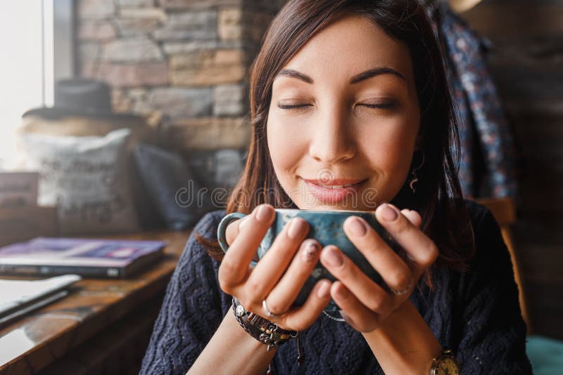 Beautiful asian woman drinking hot coffee or tea from vintage cup in modern loft cafe