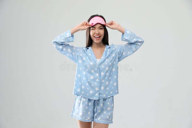 Beautiful Asian woman wearing pajamas and sleeping mask on grey background. Bedtime