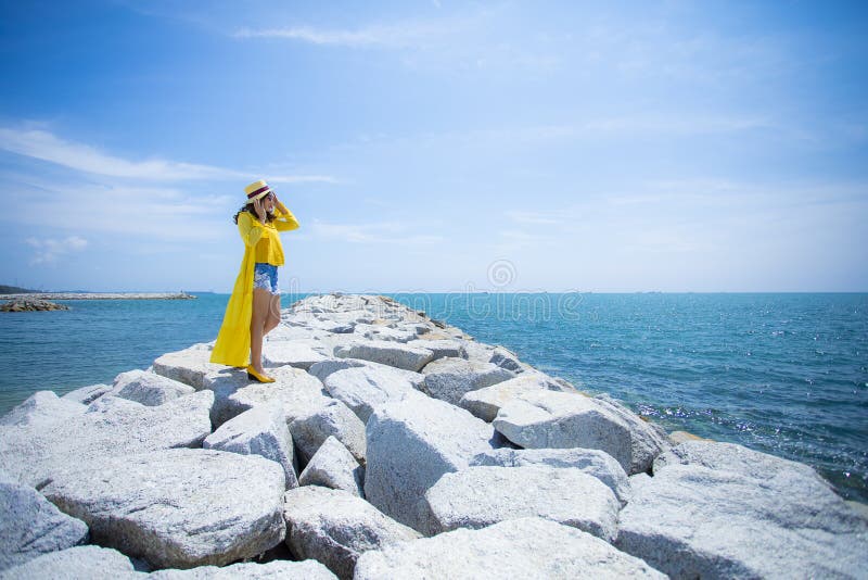 Beautiful asian woman wearing yellow clothes standing on sea beach against midday sun light