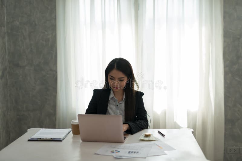 Beautiful asian young businesswoman working on laptop in her workstation.