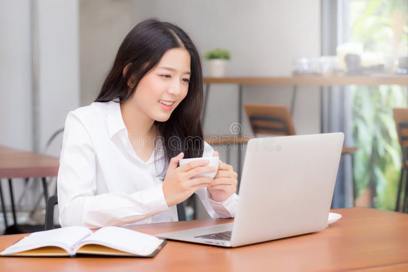 Beautiful asian young woman working online on laptop sitting at coffee shop