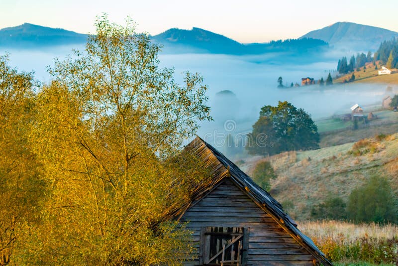 Beautiful autumn landscape during sunrise with old hut and fog in valley with mountains, Romania