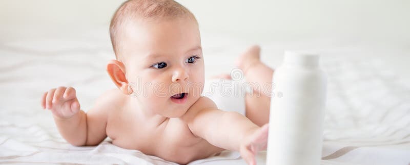 Beautiful baby holding a bottle hand care lotion tummy time bright bed airy isolated with copy space banner care stock photography Beautiful baby holding a bottle hand care lotion tummy time bright bed airy isolated with copy space banner care stock photography