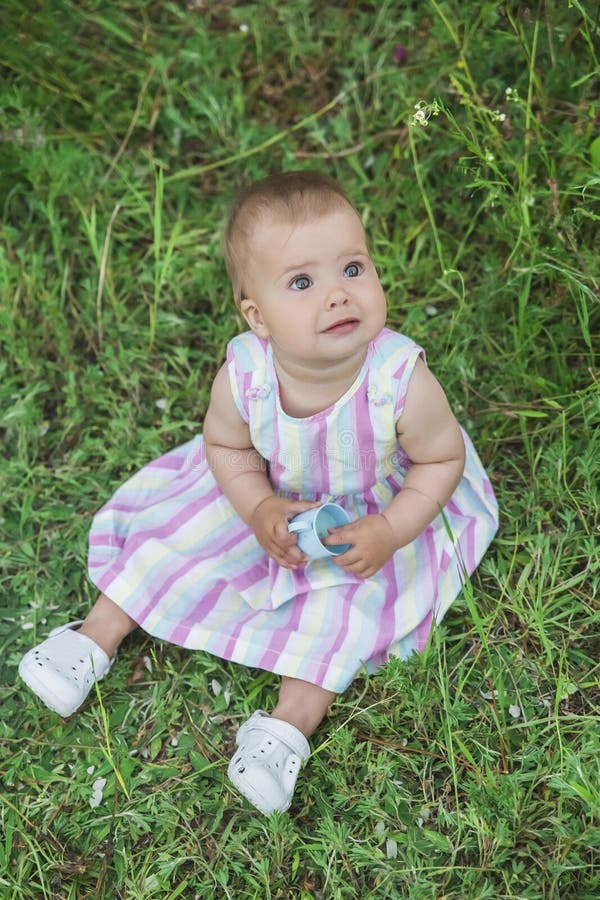 Beautiful Baby in a Striped Multi-colored Dress Sitting in a Field on ...