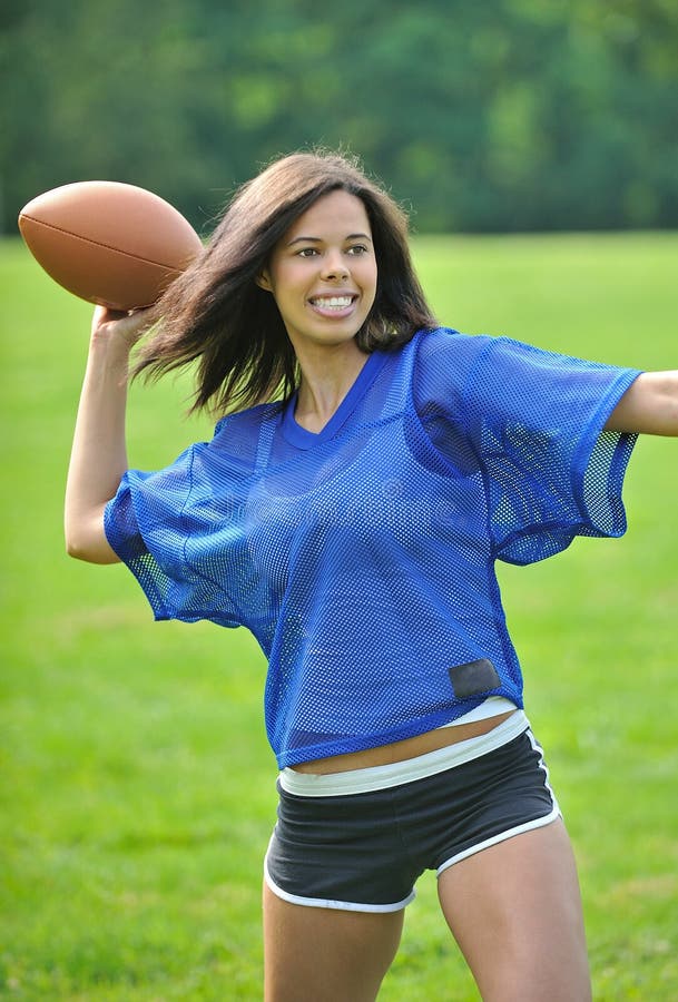 Stunning young biracial (African American and Caucasian) woman football (American) player smiling in blue mesh jersey - throwing a pass. Stunning young biracial (African American and Caucasian) woman football (American) player smiling in blue mesh jersey - throwing a pass