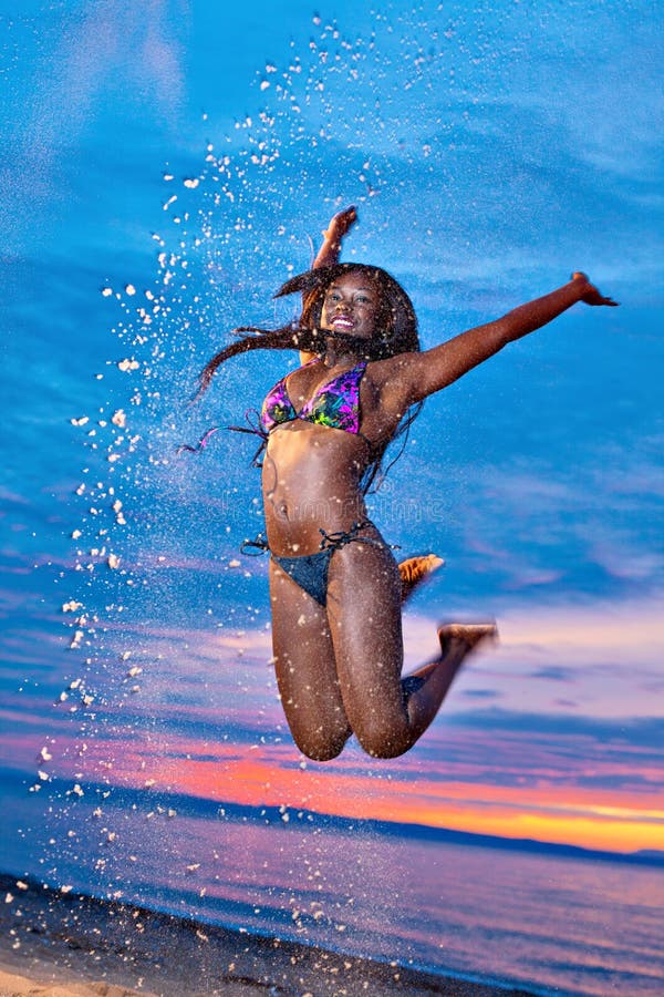 Beautiful black African American woman jumping up the air on the beach at sunset. Beautiful black African American woman jumping up the air on the beach at sunset