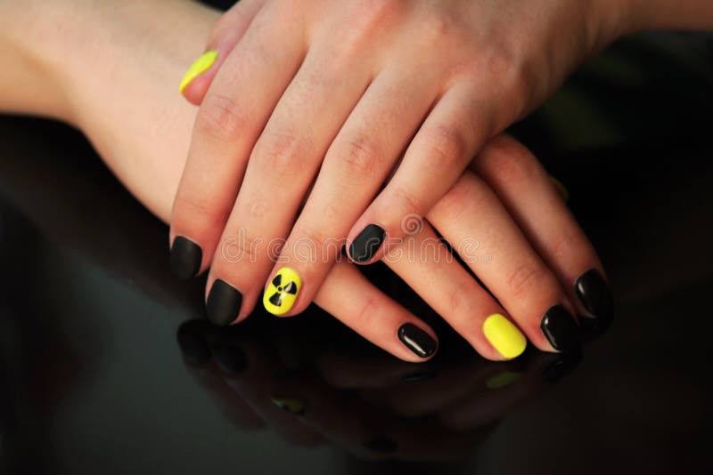 Beautiful black-and-yellow manicure with shellac varnish in the form of a sign of radioactive danger. hands of the girl on a black shiny background.