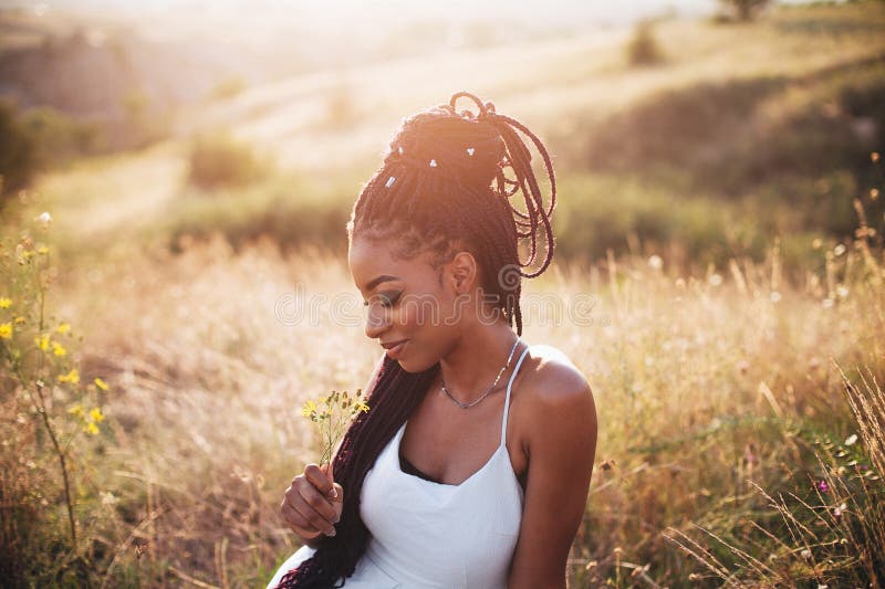 Beautiful black young woman in the park portrait long braids smiling flower