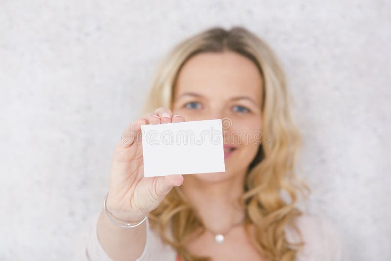 Beautiful blond woman is holding white card for copy space in front of grey background royalty free stock photo