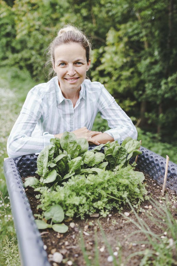 Beautiful blond woman posing next to raised garden bed and her fresh vegetables royalty free stock photography
