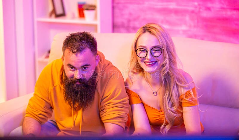 Premium AI Image  bearded boyfriend playing online games with his  beautiful blonde girlfriend sitting on their couch using wireless  controllers
