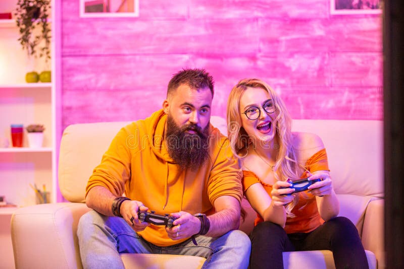 Premium AI Image  bearded boyfriend playing online games with his  beautiful blonde girlfriend sitting on their couch using wireless  controllers