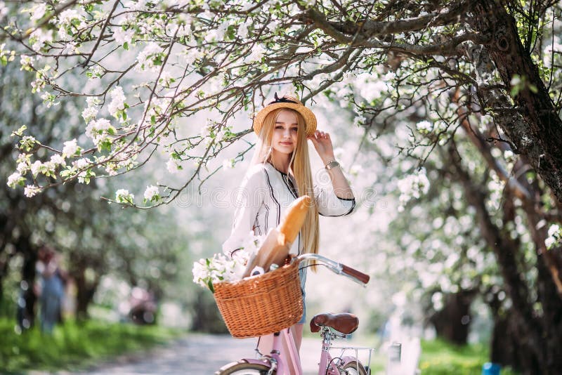 Beautiful Blonde Girl Stands on the Garden Background with a White   Holds a Bicycle with a Basket of Flowers, and Smiles Stock Image  - Image of happy, lifestyle: 123083917