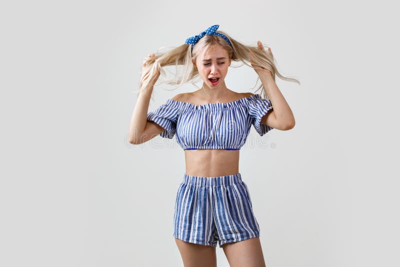 Beautiful blonde girl in summer outfit is holding hands on head crying or whining, yelling while being offended or stock photos Beautiful blonde girl in summer outfit is holding hands on head crying or whining, yelling while being offended or stock photos