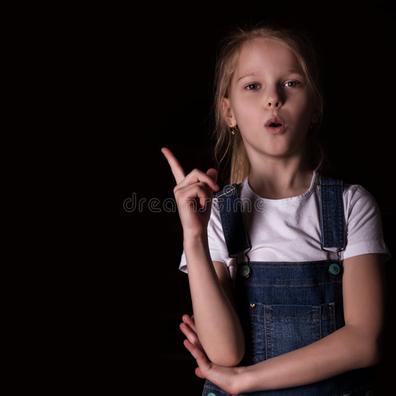 Beautiful Blonde Little Girl On A Dark Background. She Stands In ...