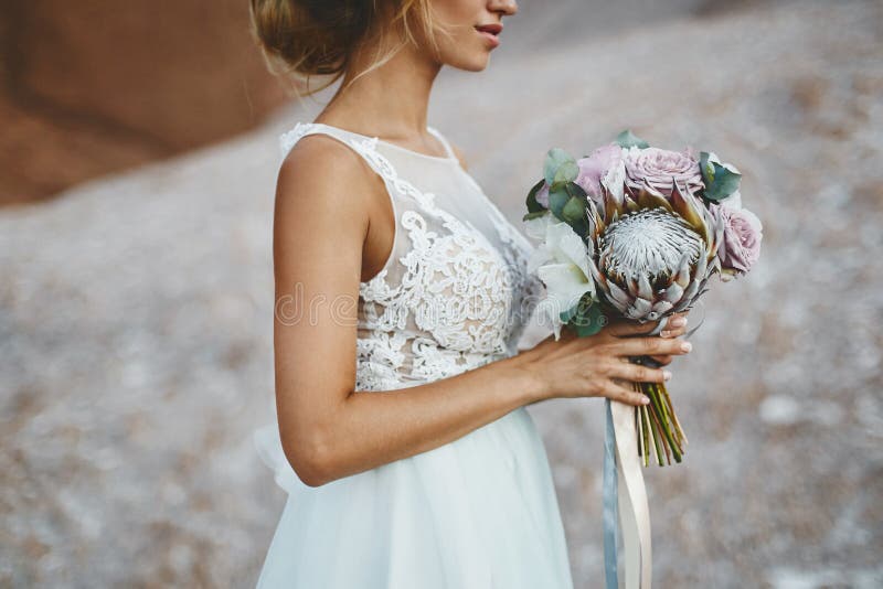 Beautiful blonde model girl with modeling wedding hairstyle in a fashionable white lace dress with a bouquet of exotics royalty free stock photography Beautiful blonde model girl with modeling wedding hairstyle in a fashionable white lace dress with a bouquet of exotics royalty free stock photography