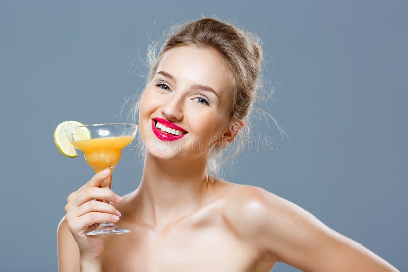 Beautiful blonde naked girl smiling, holding cocktail over grey background....