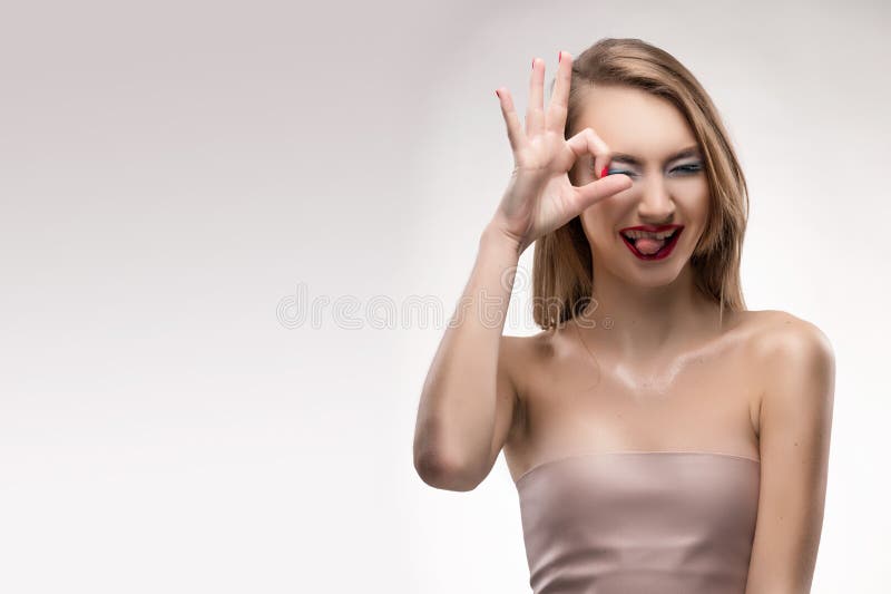 The beautiful blonde red lips smiling girl shows the sign ok, sq royalty free stock photo The beautiful blonde red lips smiling girl shows the sign ok, sq royalty free stock photo