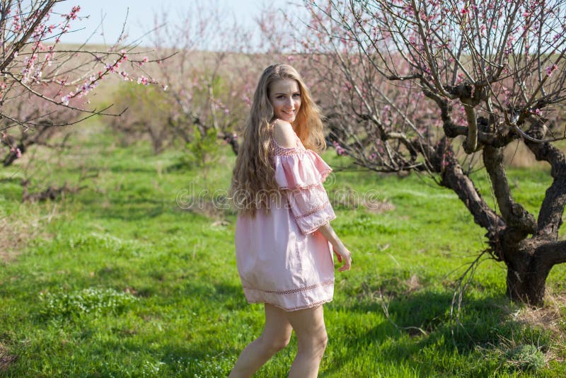 Beautiful blonde woman in a flowered Peach Garden in spring with pink flowers