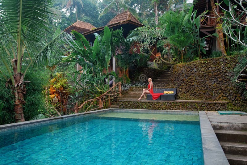 Woman in the red dress sitting on the tropical balcony near the pool