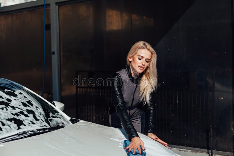 Beautiful blonde woman washes with rag with foam white car at car wash