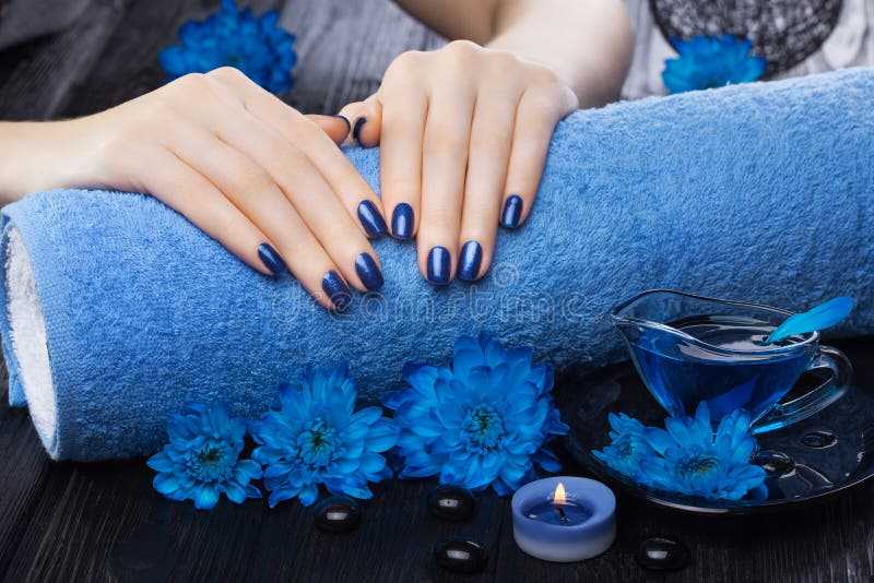 Beautiful blue manicure with chrysanthemum and towel on the black wooden table. spa royalty free stock photo