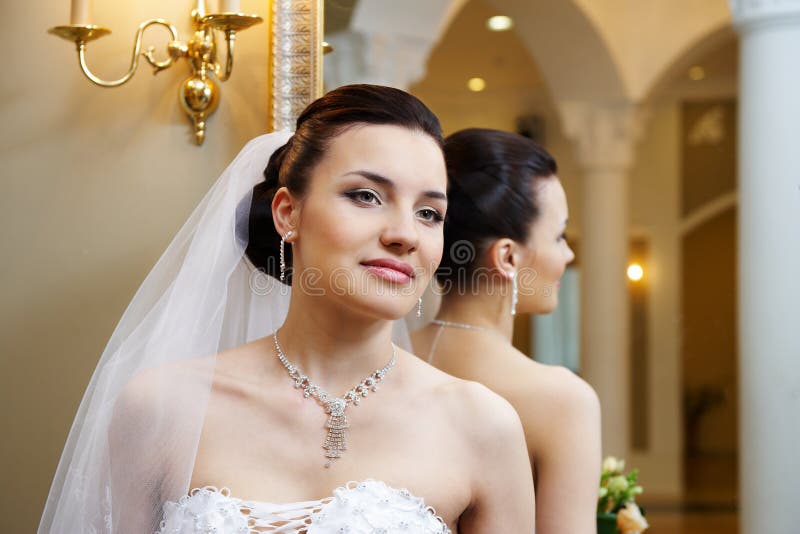 Beautiful bride near mirror in wedding palace