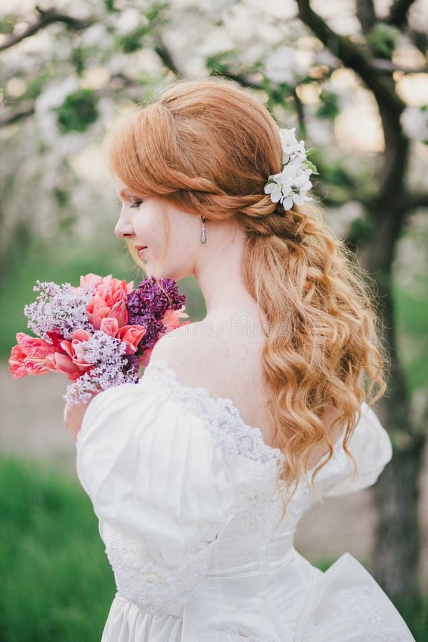 Beautiful bride in a vintage wedding dress posing in a blooming apple garden. Spring mood. Young woman in a white vintage dress