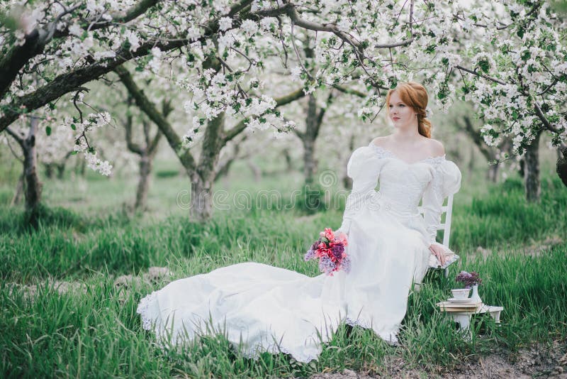 Beautiful bride in a vintage wedding dress posing in a blooming apple garden. Spring mood. Young woman in a white vintage dress